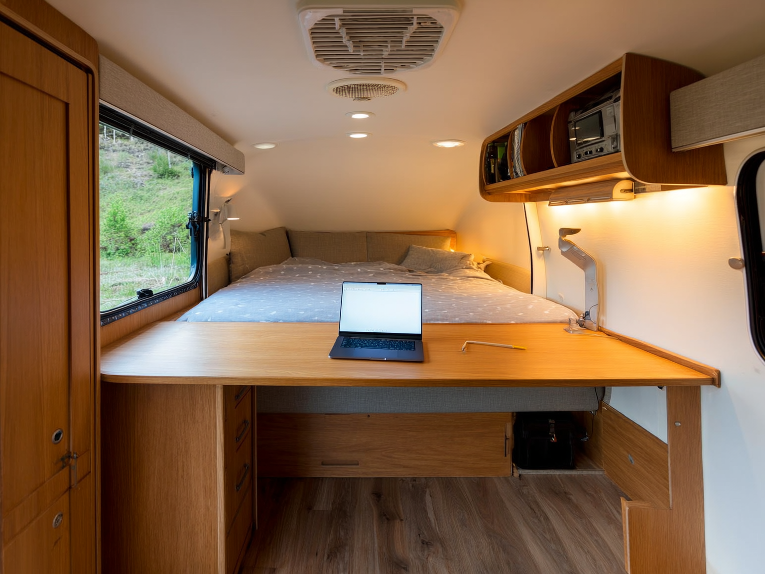 Interior of a well-organized RV set up as a comfortable home office with a laptop and warm lighting, lived-in and tidy, no people